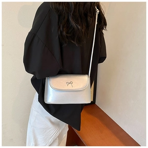 Detail of silver metallic crossbody bag featuring a delicate gold bow metal buckle