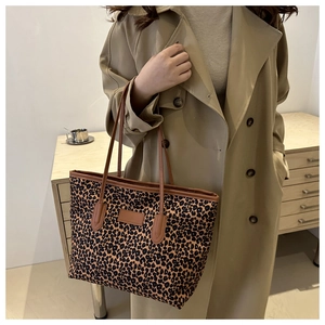 Close-up of a large leopard print tote bag with brown leather handles in a home setting