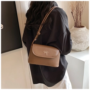 Gros plan d'un sac en cuir marron avec fermoir noeud doré et détail de bandoulière nouée