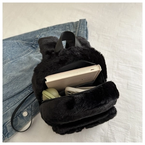 Interior capacity view of small black plush backpack showing daily essentials and soft texture