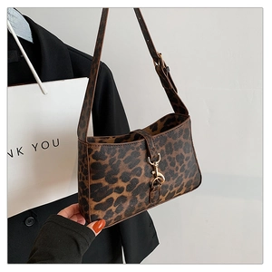 Detail of leopard print shoulder bag featuring gold clasp held by a model in a chic setting