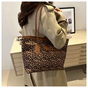 Detailed view of leopard print tote bag with brown straps worn by a model in a warm setting