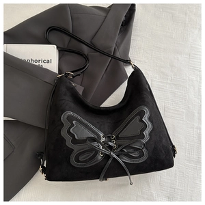 Detail of suede crossbody bag featuring a large leather butterfly patch and lacing