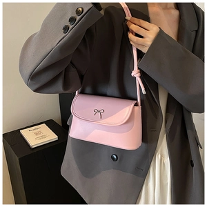 Détail d'un sac bandoulière en cuir rose orné d'un délicat nœud métallique sur le rabat