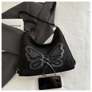 Detail of black suede tote bag featuring a large butterfly patch and lace-up design