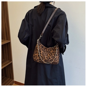 Close-up of leopard print shoulder bag with gold chain strap on black trench coat