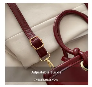 Detail of dark red bucket bag featuring shiny texture and gold adjustable metal buckle