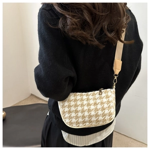 Detail of houndstooth plaid crossbody bag with wide strap and gold hooks on shoulder