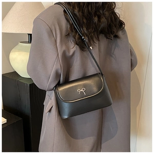 Close-up of black matte leather square bag with silver metal bow detail on grey blazer