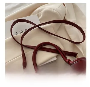 Close-up of glossy burgundy leather bucket bag strap with gold metal eyelets