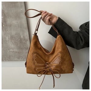 Detail of brown suede tote bag featuring decorative leather butterfly patch and lacing