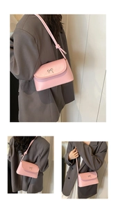 Detail of pink crossbody bag with metal bow accent and slim strap on grey blazer