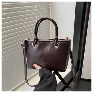 Detail of glossy coffee brown leather bucket bag with gold hardware and top handle