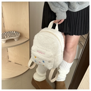 Detail of white plush backpack featuring colorful studs and pink FASHION embroidery