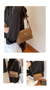 Close-up of a dark brown leather crossbody bag with a silver bow buckle on the front flap