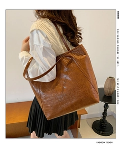 Macro detail of brown crocodile pattern faux leather tote bag on a female model