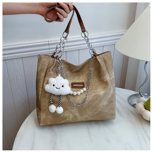 Detail of tan canvas tote bag featuring silver chain strap and plush cloud charm