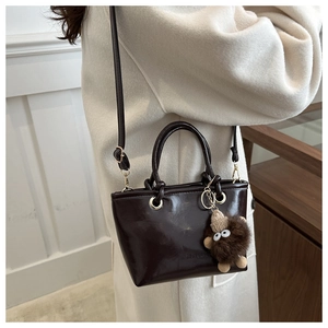 Detail of dark brown glossy bucket bag with cylindrical handles and plush monster charm