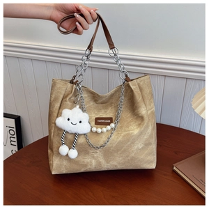 Detail of canvas tote bag featuring a plush cloud charm and pearl chain shoulder strap