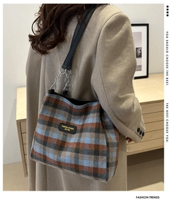 Detail of plaid wool tote bag featuring a leather brand tag and metal chain strap