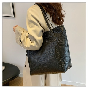 Detailed side view of black crocodile pattern tote bag with slender straps on model shoulder