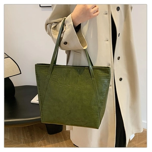 Detail of dark green crocodile texture on a large tote bag carried by a model
