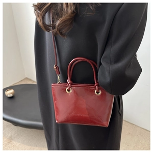 Detailed side view of burgundy patent leather bucket bag worn by model for scale