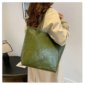 Detail of olive green tote bag with crocodile texture and shoulder strap on model