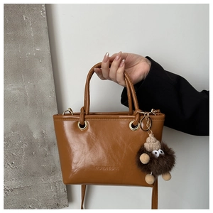 Detail der braunen glänzenden Leder-Eimertasche mit Prägung und Plüsch-Monster-Anhänger
