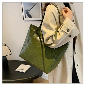 Close-up of green crocodile-pattern tote bag shown in a stylish urban office setting