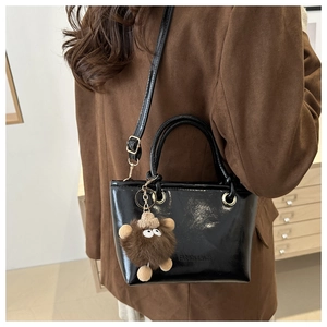 Detail der schwarzen Lack-Eimertasche mit Trageriemen und süßem braunem Plüschbär-Anhänger