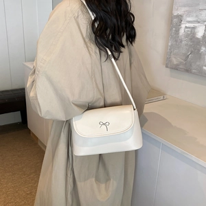 Stylish cream white crossbody bag with silver bow accent worn by a model in a minimal setting