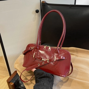 Detail view of burgundy patent leather handbag featuring gold zipper and retro belt strap