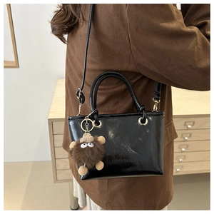 Detail einer schwarzen Lackleder-Eimertasche mit Bärenanhänger und Mode-Schriftzug