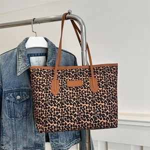 Large leopard print tote bag with brown faux leather trim hanging on a metal rack