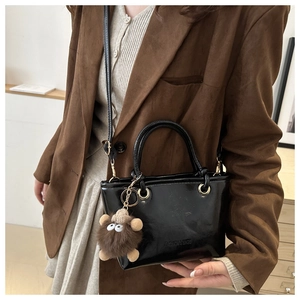 Detailansicht schwarze Lackleder-Beuteltasche mit braunem Plüschanhänger und Riemen