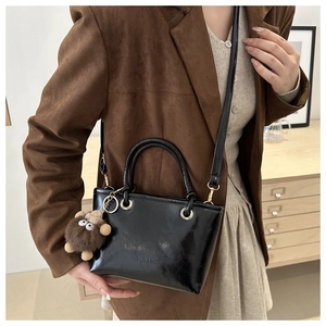 Detail of black glossy bucket bag with golden hardware and plush animal charm