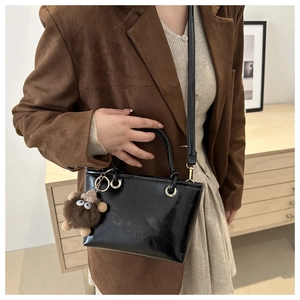 Detail of glossy black shoulder bag with plush monster charm on model in brown suit