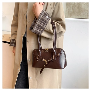 Detail of dark brown patent leather tote bag with gold hardware shown on a model
