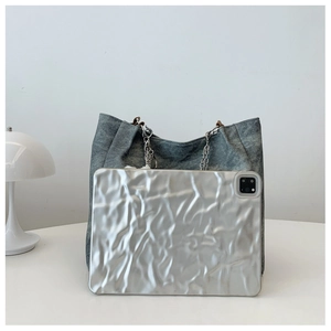 Detail of dark gray denim tote bag with chain strap next to a silver tablet for scale