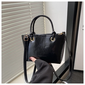 Detail of glossy black leather bucket bag featuring elegant gold hardware and thin straps