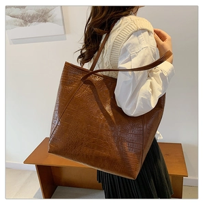 Side view of large brown crocodile embossed tote bag worn by a model in a room