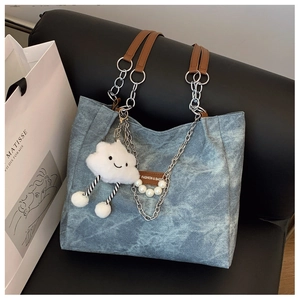 Detail of washed blue denim tote bag featuring silver chain and white plush cloud charm
