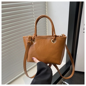 Close-up of bright brown bucket bag with FASHION & BAGS engraving and gold hardware