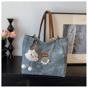 Detail of blue denim tote bag with brown leather handles, pearl chain and cloud charm