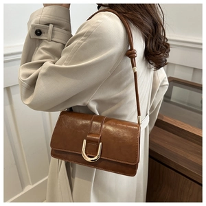 Detail of a brown leather shoulder bag with gold buckle and knotted strap on an outfit