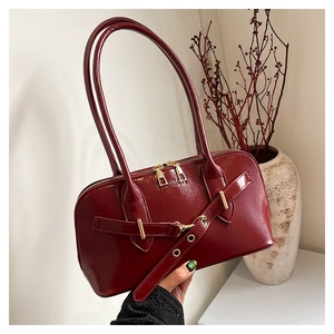 Close-up of a deep red glossy shell bag with gold double zippers and embossed fashion logo
