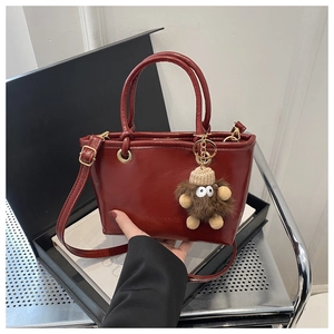 Detailansicht der weinroten Eimertasche mit Mode-Logo und Plüsch-Monster-Anhänger-Dekoration