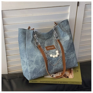 Detail of blue denim tote bag featuring dual brown leather straps and pearl chain accent
