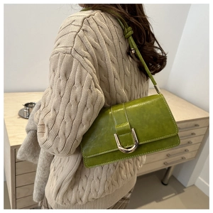 Détail du sac à bandoulière en cuir vert avec boucle en U argentée sur pull en maille beige